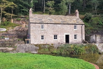 aqueduct cottage in the sunshine with the woods behind and a lawn in front