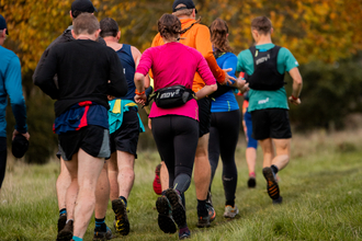 runners in an array of colours running through a field with autumnal trees in the background