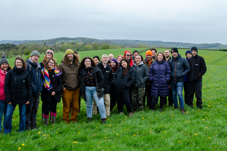 a group of people stood together in a field smiling at the camera with a grey sky