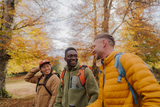 Three people walking together through a woodland smiling and laughing with each other 