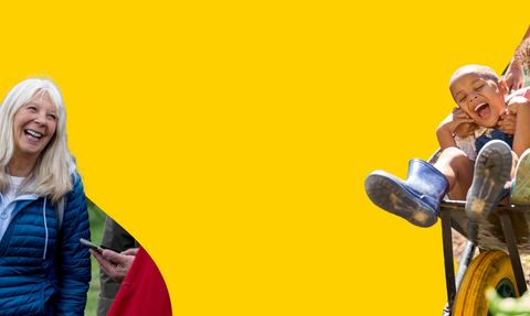 A multi-generational group of people enjoying an outdoor activity. An older woman laughs while looking to the left, children are being pushed in a wheelbarrow, and an adult is holding a phone, all against a bright yellow background.