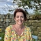 A woman in a colourful top sat on a blue chair in front of a dry stone wall and a blue sky