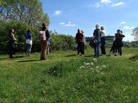 a group of people stood with their back to the camera in a grassy field on a sunny day