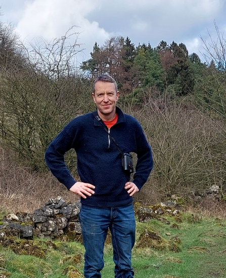 An image of a man with binoculars stood outside in nature