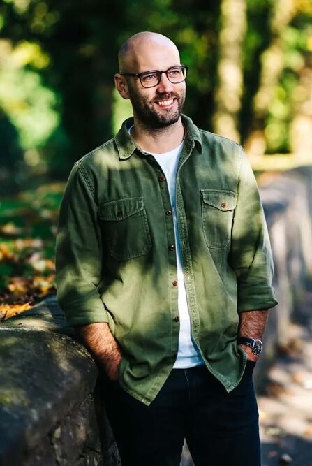 Image of a man wearing glasses stood in nature